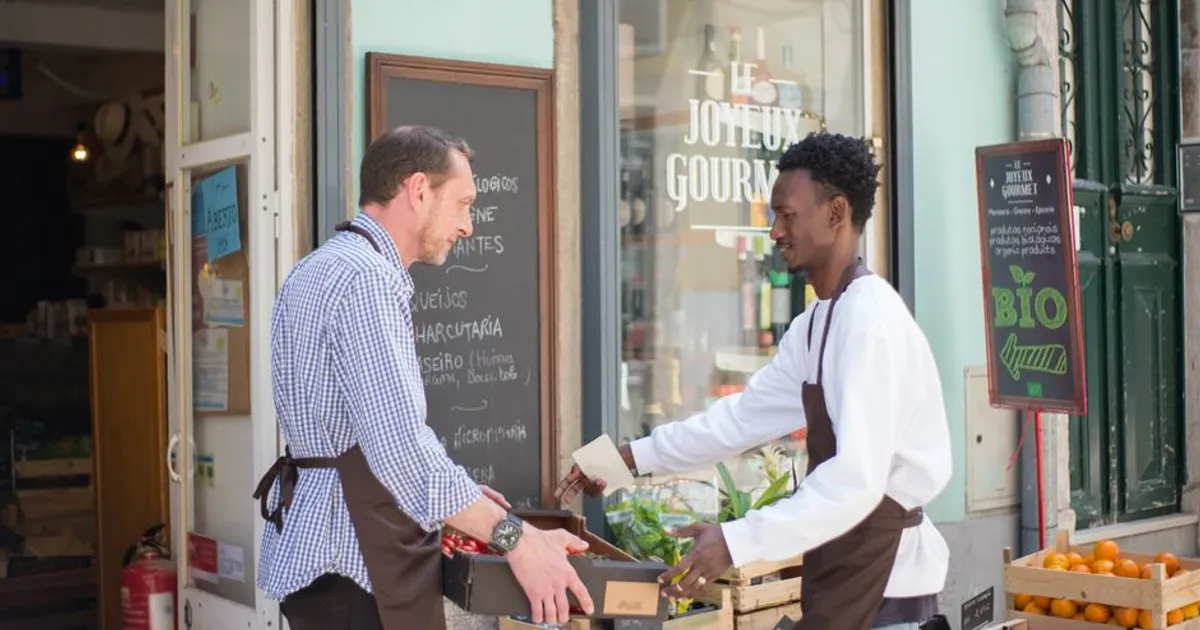 Two men arranging fruits and vegetables outside a store in Portugal.