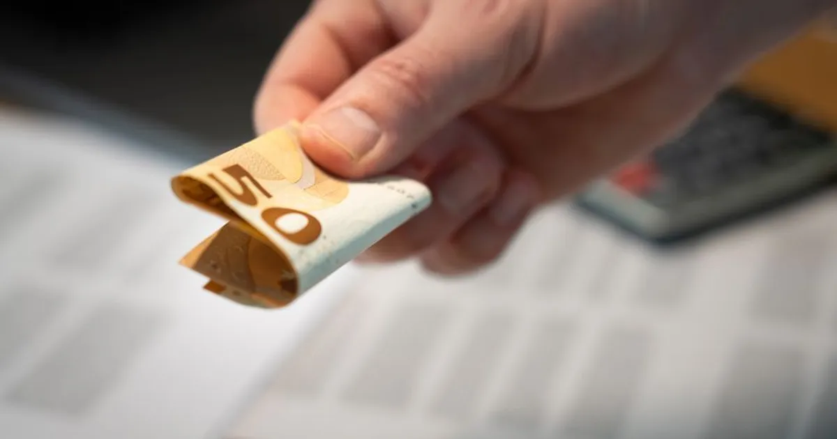 A detailed image of a hand holding a folded 50 euro banknote, with documents in the background.