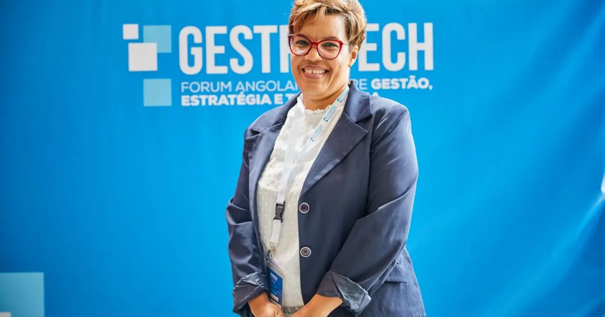 Businesswoman smiling in front of blue backdrop at trade fair event, embodying leadership and professionalism.