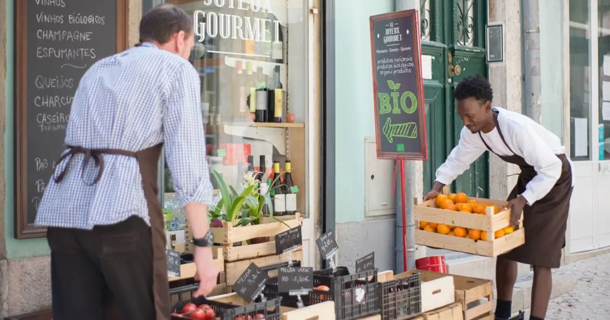 Two vendors organizing organic fruits and vegetables at a street market in Portugal.