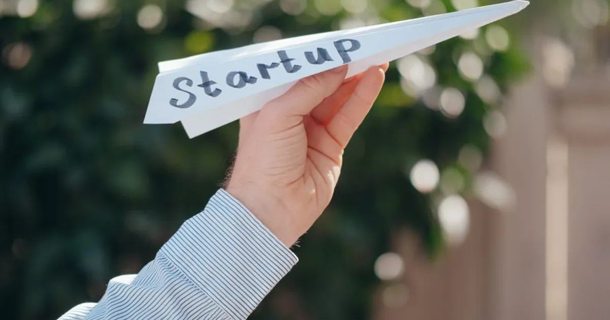Close-up of a hand holding a paper plane with 'Startup' written, symbolizing a business launch.