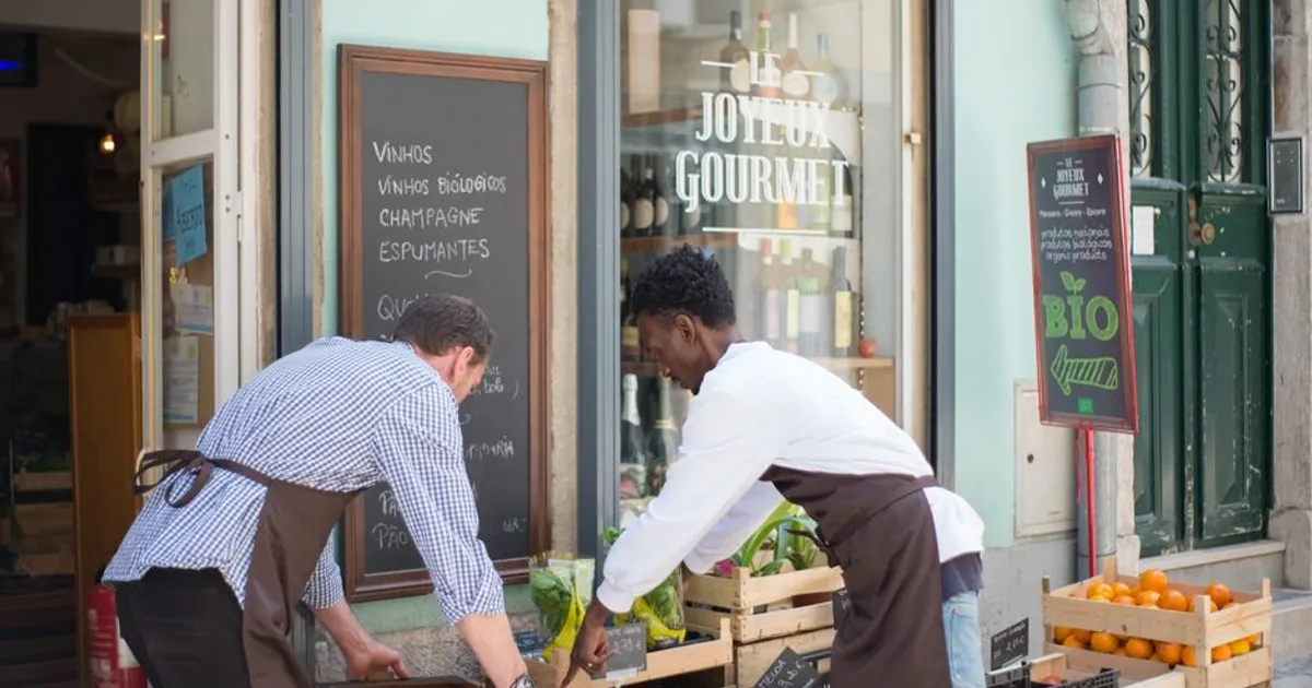 Two men organizing produce outside a gourmet store in Portugal on a sunny day.