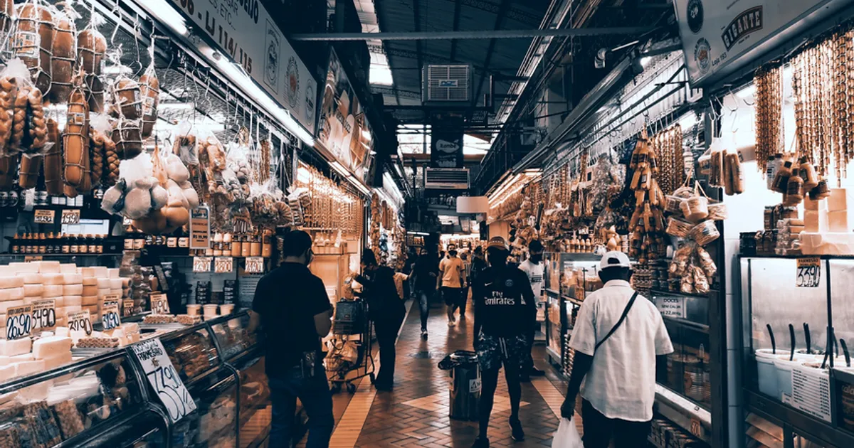A bustling indoor market aisle filled with diverse shops and people shopping.
