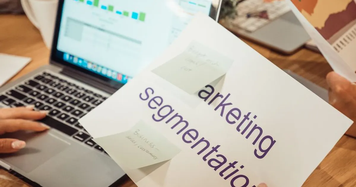 A modern workspace showing hands analyzing marketing data on a laptop and paper documents.