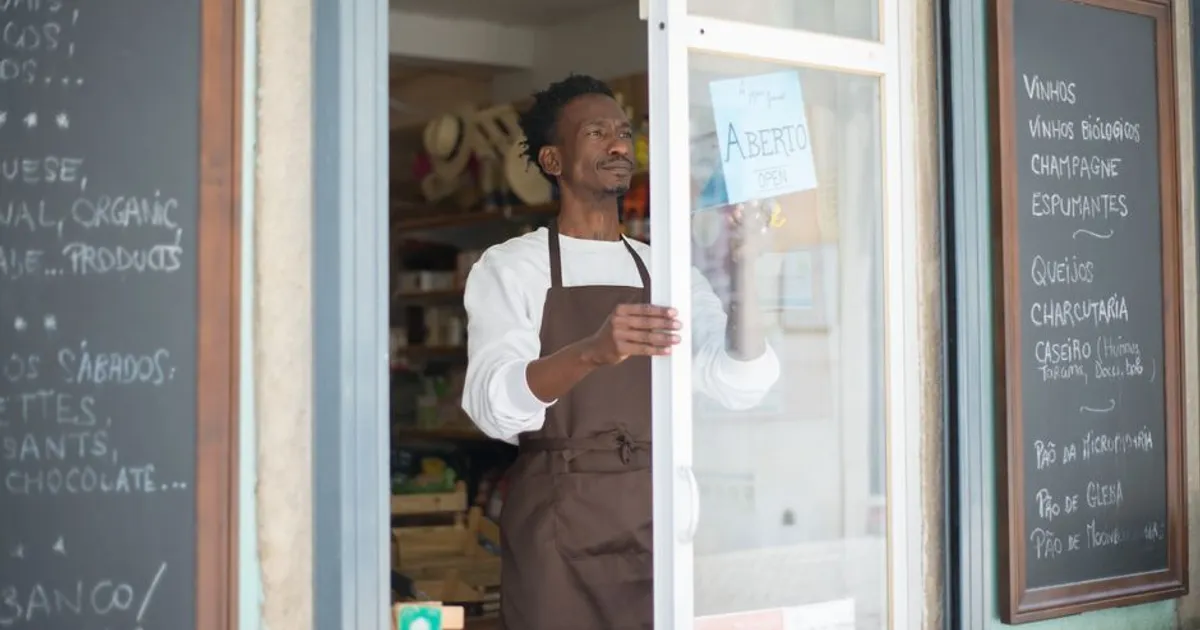 A man in an apron opens a grocery store door in Portugal, ready for business.