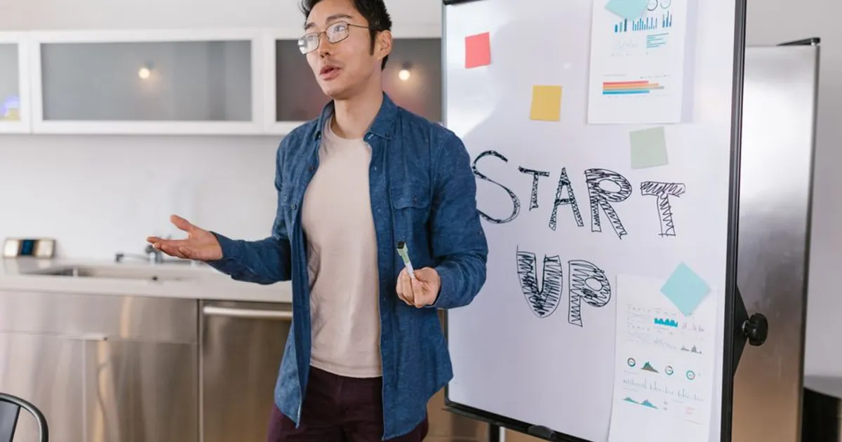 Asian businessman presenting a startup idea with charts and graphs on a whiteboard.