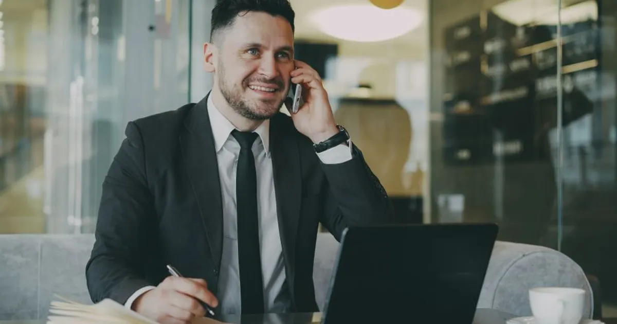 Professional man in a suit talking on the phone and working on a laptop indoors.